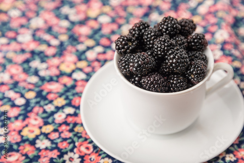 Blackberry berries in a white cup closeup on a color blurred background