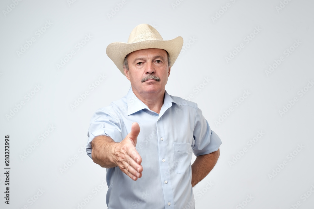 Portrait of serious american mature man in cowboy hat stretching hand for shaking to welcome someone Portrait of serious american mature man in cowboy hat stretching hand for shaking to welcome someone