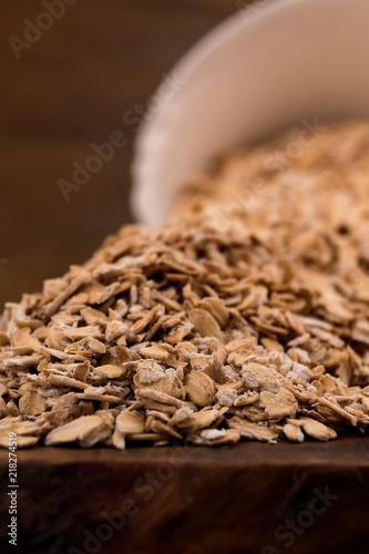Oat flakes on the table, scattered from a fallen white bowl, close - up on a wooden background.