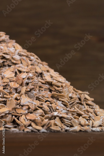 Half a pile of oat flakes, sprinkled with a slide on a wooden table, close-up.