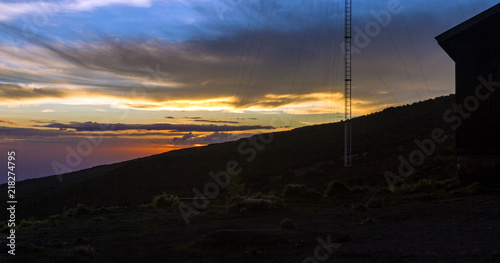Multi-colored sunset on the mountainside with a campers hut and a radio tower in silhouette