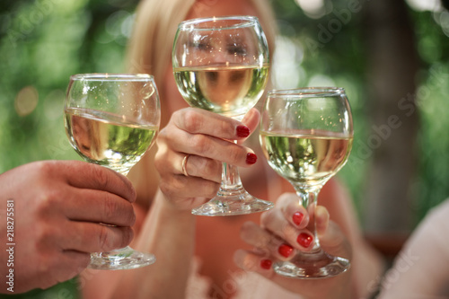 Closeup photo of hands clinking glasses with white wine,