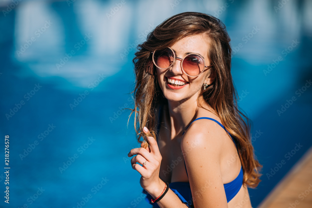 Close up fashion portrait of sensual smiling beauty brunette woman posing in swimming pool, relaxing enjoy her summer vacation.hot summer fashion accessory,stylish sunglasses,bikini.