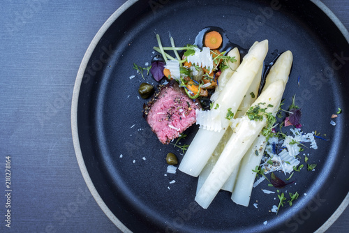 Modern style Italian barbecue dry aged tagliata di manzo with white asparagus and parmesan as top view on a plate with copy space left
