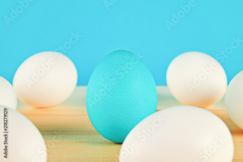 Fotografía The blue egg won among the white eggs on the wooden table.