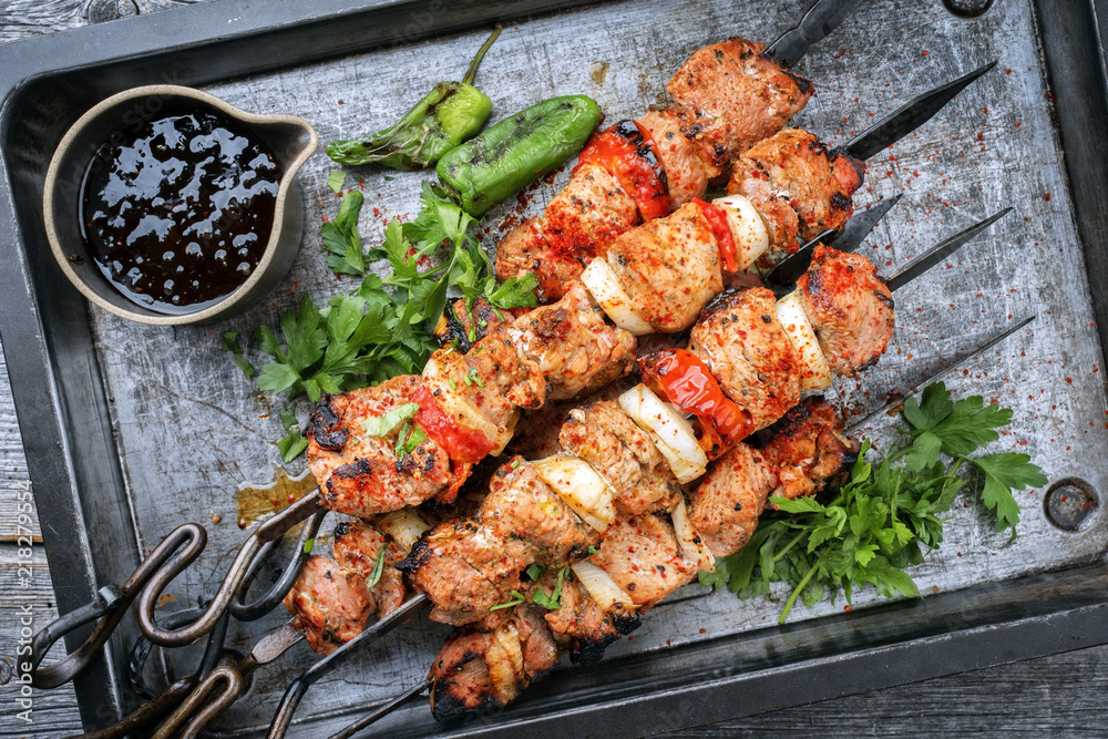 Traditional Greek souvlaki barbecue skewer with tomato, onion and paprika as closeup on a metal griddle