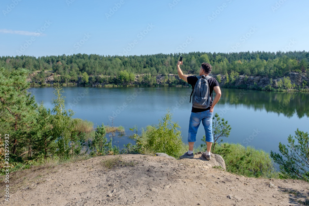 Senior white man with backpack stands on the rock and making selfie