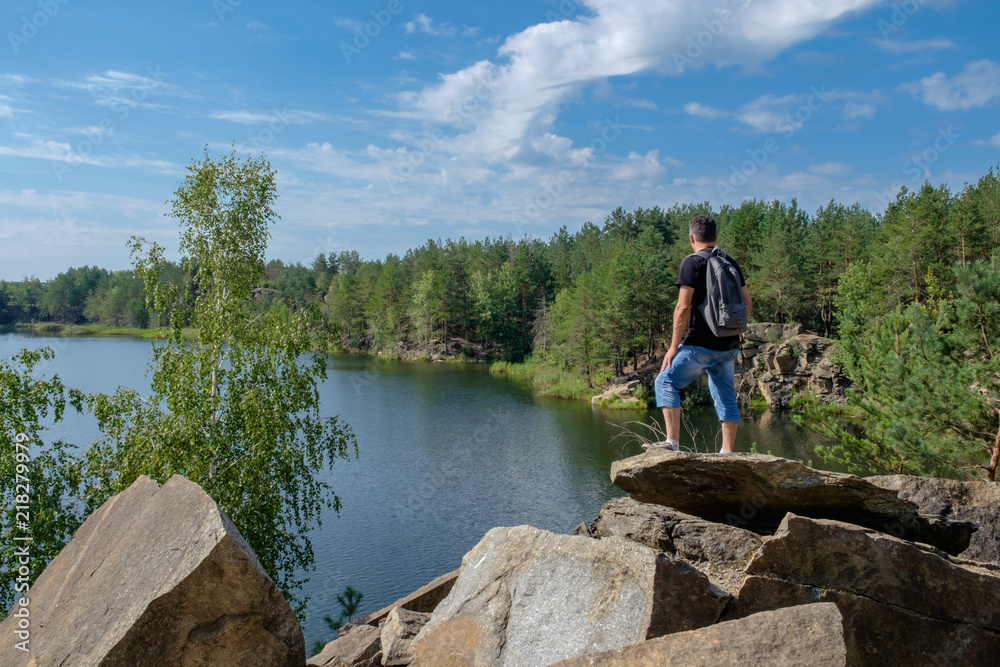 Adult white man with backpack stands on the rock and looks at the lake