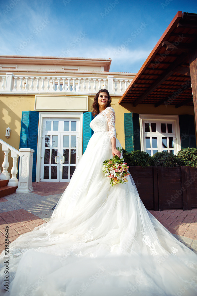 Obraz premium A beautiful bride in a white wedding dress and with a bouquet of flowers enjoying the moment. Wonderful mood, beautiful waves, great atmosphere. wedding concept.