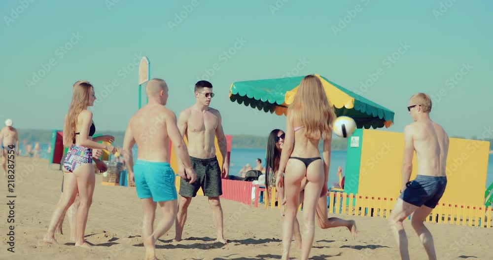 Group of carefree guys and teenage girls enjoying beach volleyball on the sand