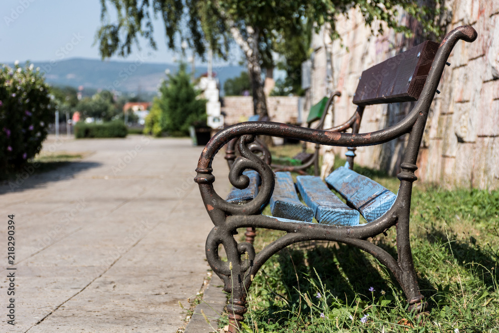 Wooden bench for relaxation in summer weather in park on sunny day. Stylish bench is empty and nobody. Close up, selective focus Wooden bench for relaxation in summer weather in park on sunny day. Stylish bench is empty and nobody. Close up, selective focus