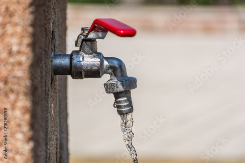 Faucet with red handle and open water outdoor on sunny summer day. Save water concept. Close up, selective focus