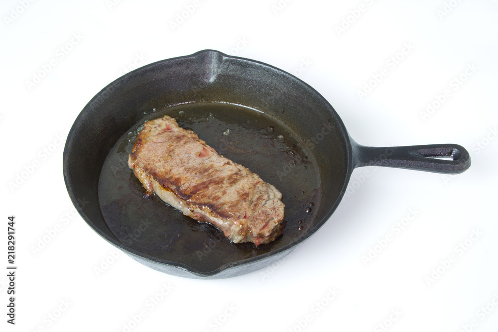 Beef Steak frying in a cast iron skillet isolated on white background