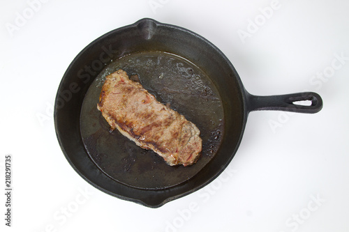 Beef Steak frying in a cast iron skillet isolated on white background