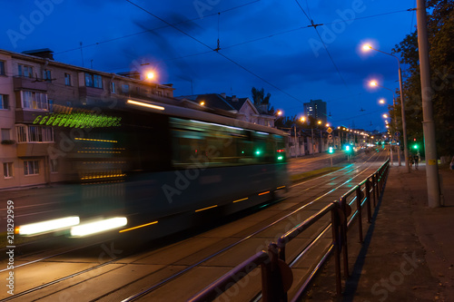 The motion of a blurred tram down the street in the evening.