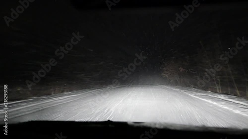 Night driving in the car in the snowfall blizzard on the snow-covered road. Bad weather. Low beam and high beam of headlighs. Road safety