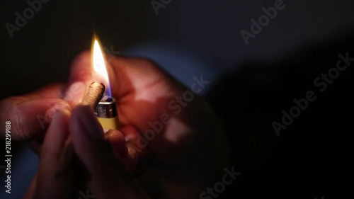 A close up of a hand lighting a blunt and the flame dances in the darkness.