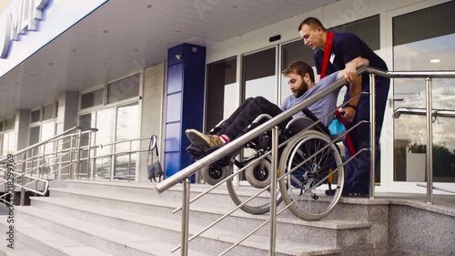 A man helping to move down the stairs to a disabled person in a wheelchair