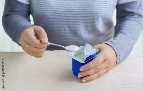 Woman holding a cup of yogurt and spoon in hand on the table. Selective focus.