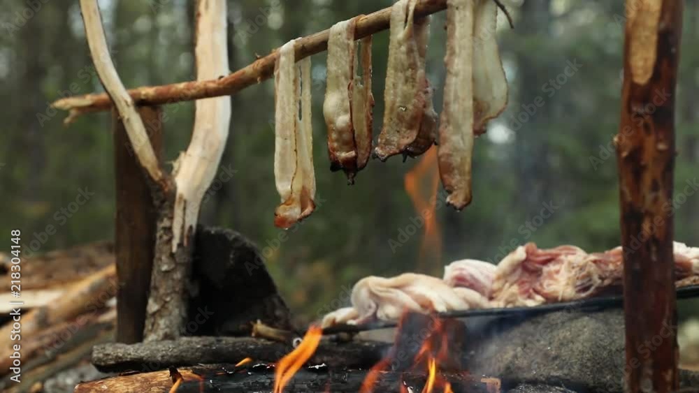 Cooking bacon over a stick while camping in the forest