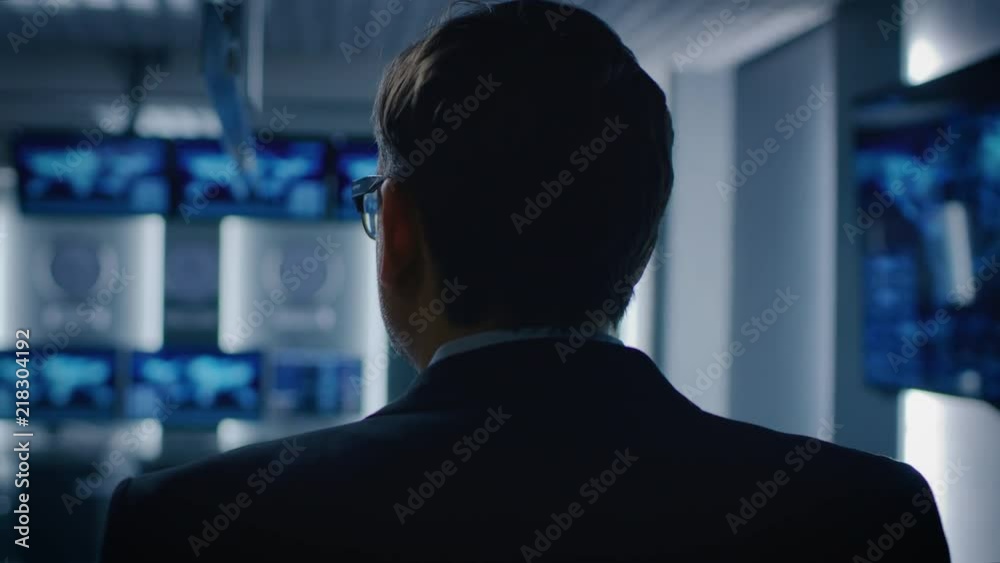 Back View Shot of the Government Official / Politician / Newsroom Reporter / Business Man Standing in the Room with Blurred Screens.