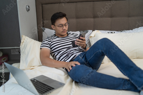 asian man using handphone and listening to music at bedroom © Kencana Studio