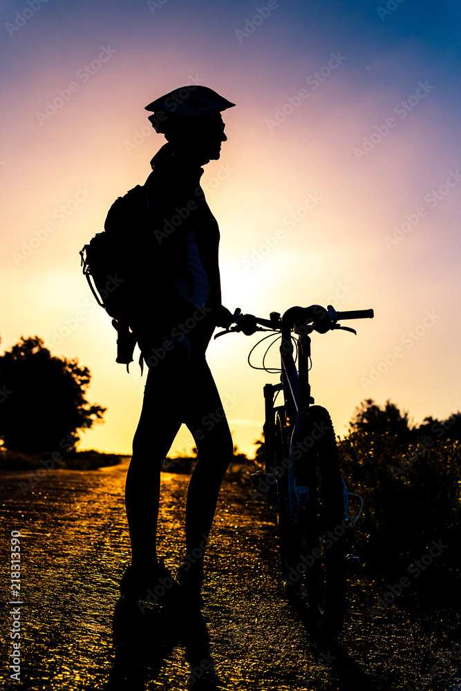 Silhouette of a girl with a bicycle at sunset in the summer