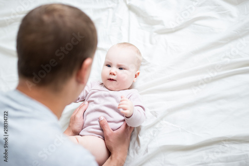 happy young father playing with baby girl at home - copy space over white sheet