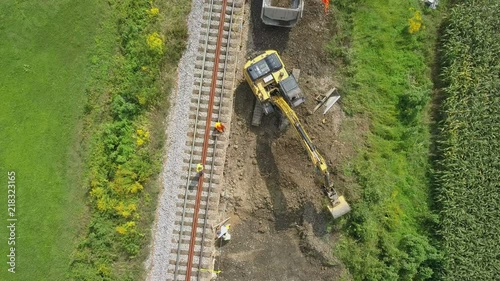 Aerial: Flying over excavator working at railway reconstruction site. Filming rails renovation at railway beside beautiful river on sunny day.
