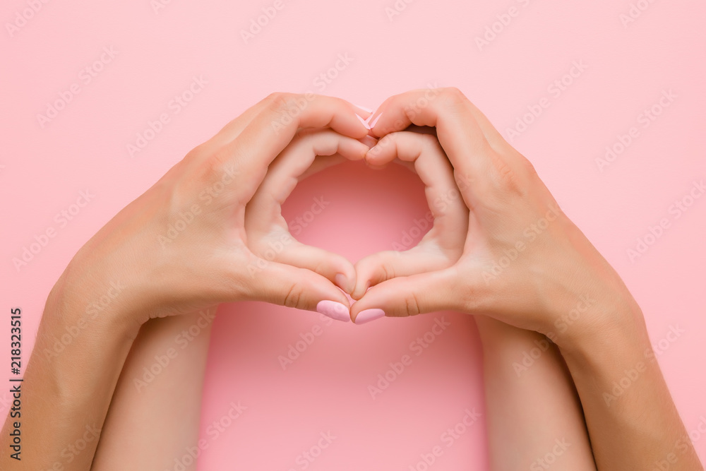 Fototapeta premium Heart shape created from little girl's hands and her mother's hands on the pink background. Lovely emotional, sentimental moment. Love, happiness and safety concept.