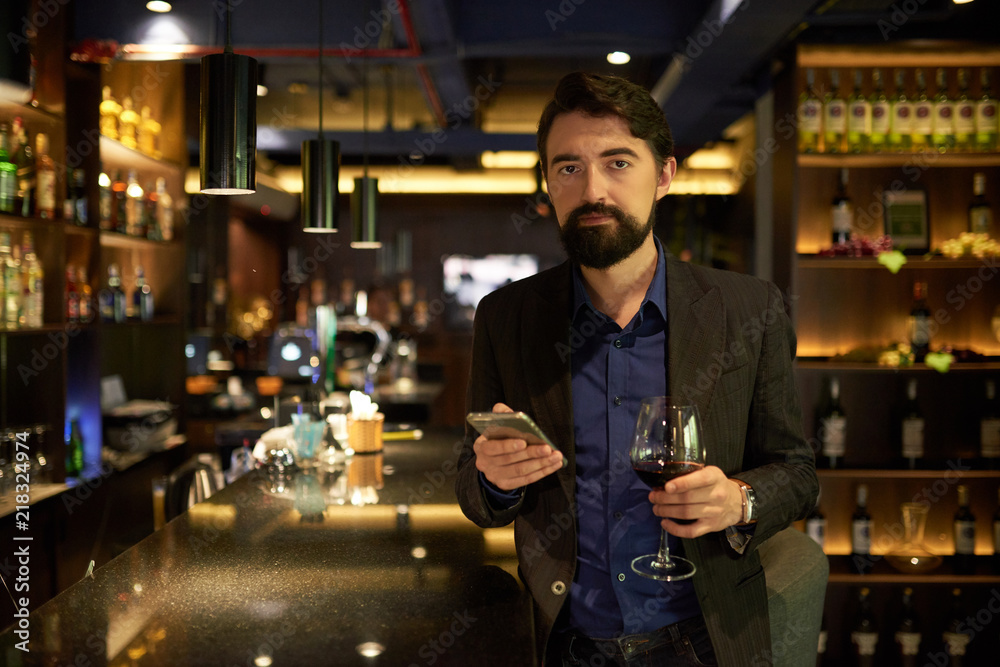 Portrait of businessman drinking glass of wine in bar after hard day at work