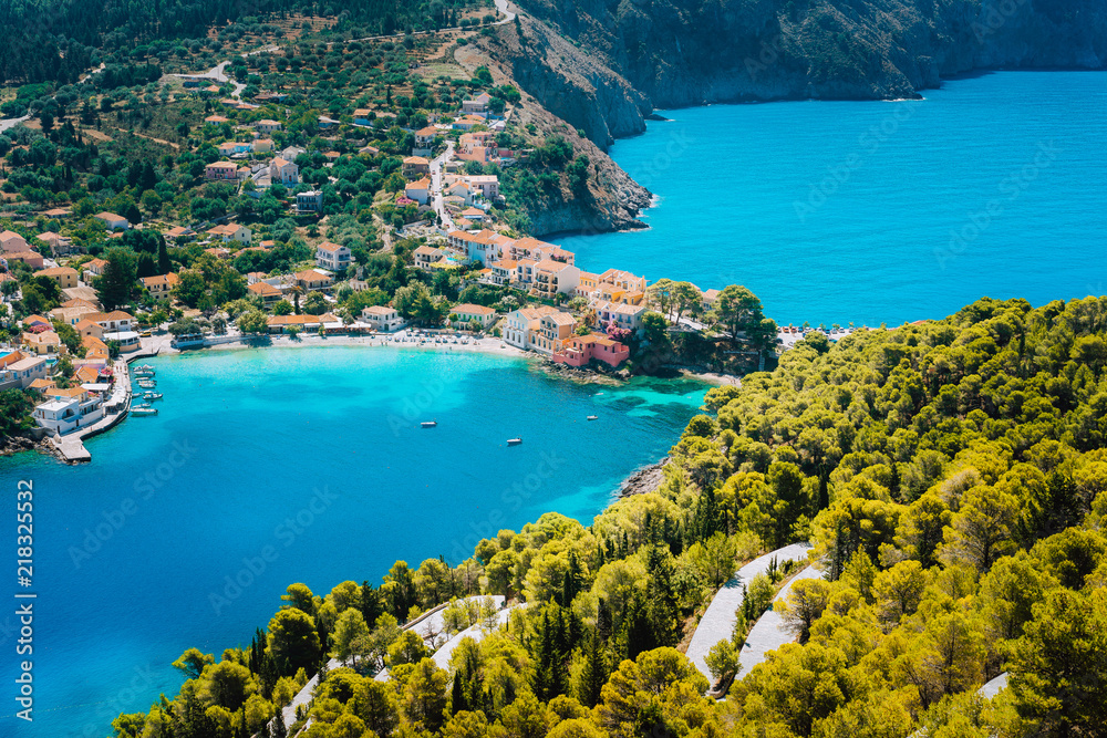 Panoramic view to Assos village Kefalonia. Greece. White lonely yacht in beautiful turquoise colored bay lagoon water surrounded by pine and cypress trees along the coastline