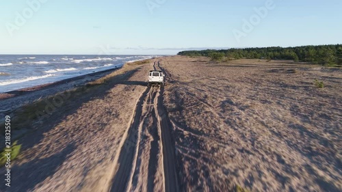 Aerial drone tracking shot of Land Rover Defender 90 driving on a sandy beach