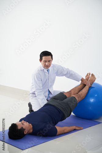 Physiotherapist putting legs of patient on fit ball during rehabilitation session