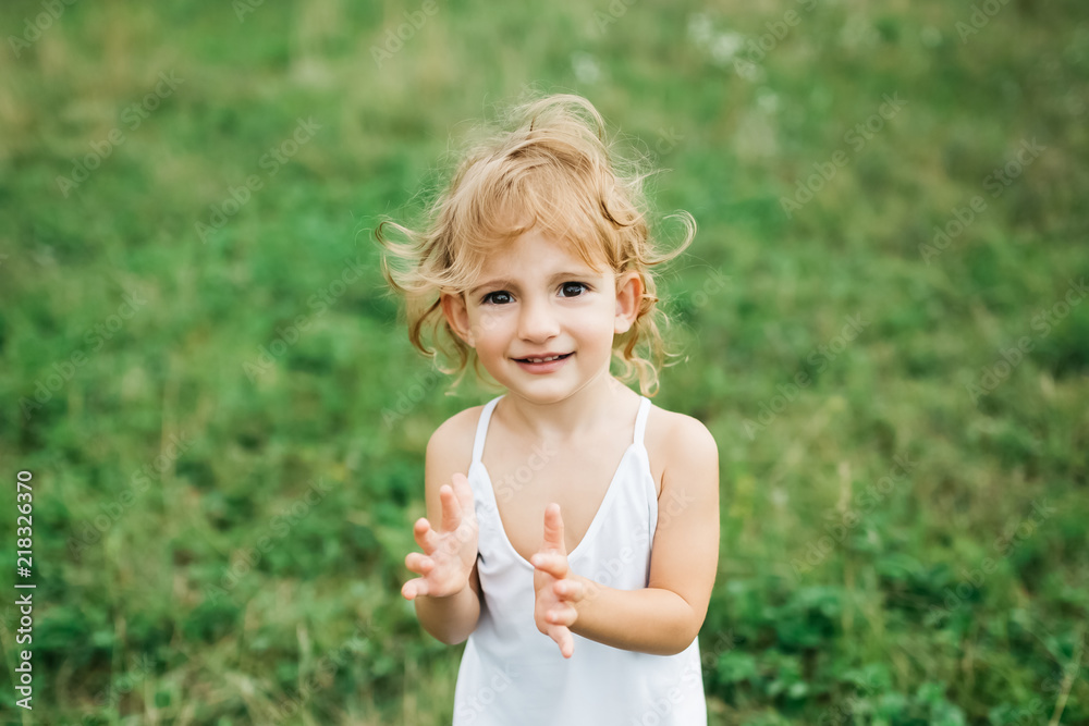 happy adorable child with curly hair looking at camera and standing on green grass