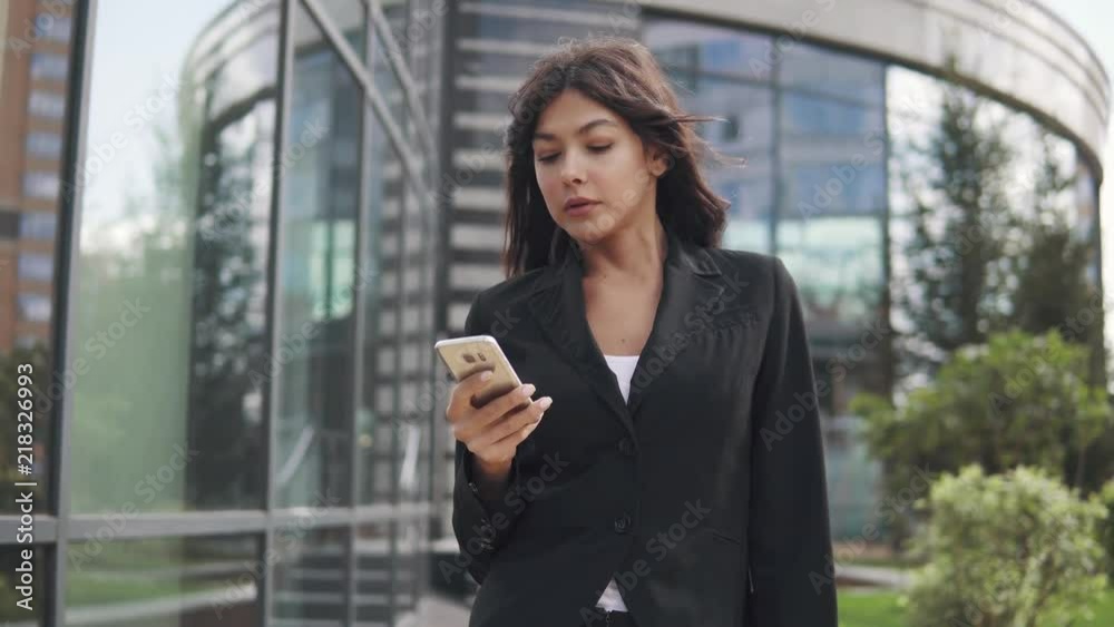 beautiful young woman in a business suit using a smartphone. business woman texting a message on a mobile phone beautiful young woman in a business suit using a smartphone. business woman texting a message on a mobile phone