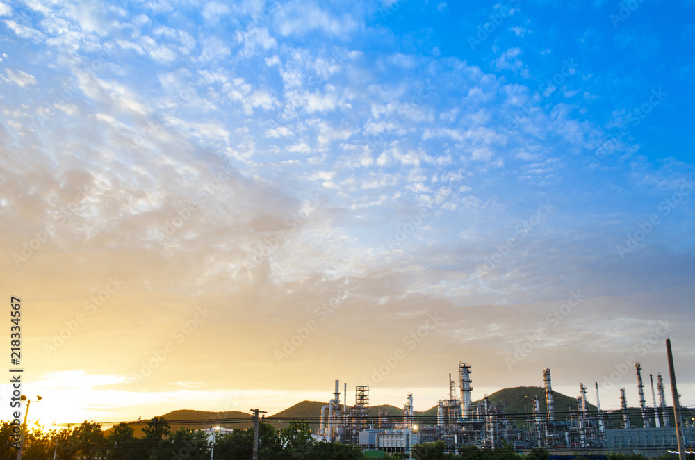 Oil refinery and sunset sky have mountain in background this sky is beautiful orange color and blue color  the refinery have a lot of chimney ,this image in energy and oil refinery concept