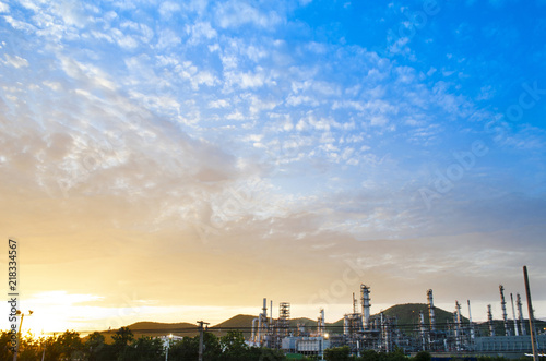 Oil refinery and sunset sky have mountain in background this sky is beautiful orange color and blue color the refinery have a lot of chimney ,this image in energy and oil refinery concept