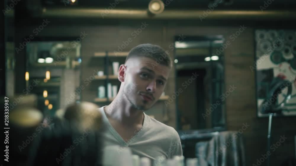 Attractive man is looking in the mirror after his haircut in barbershop, smiling and winking himself. Happy client at the hair salon after haircut Attractive man is looking in the mirror after his haircut in barbershop, smiling and winking himself. Happy client at the hair salon after haircut