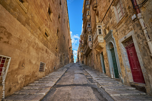 Fototapeta Naklejka Na Ścianę i Meble -  Narrow street in Valletta city going upward between big houses