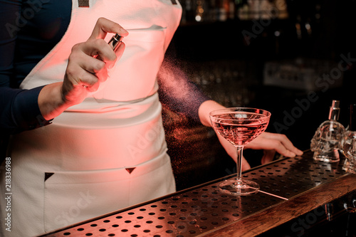 Female barman spraying bitter on the elegant cocktail glass