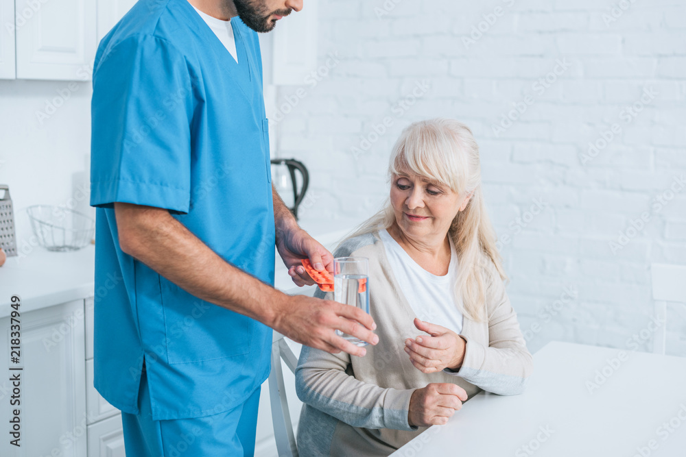 Obraz premium cropped shot of social worker giving glass of water and pills to senior woman