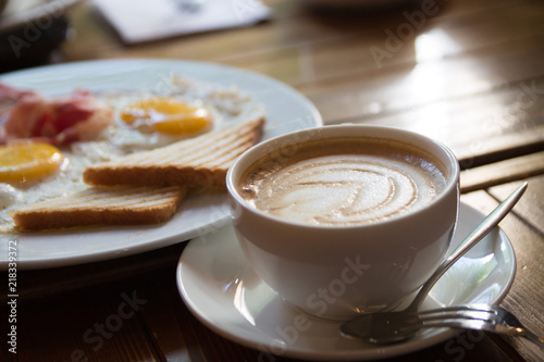 breakfast with fried eggs, bacon, toasts and cappuccino
