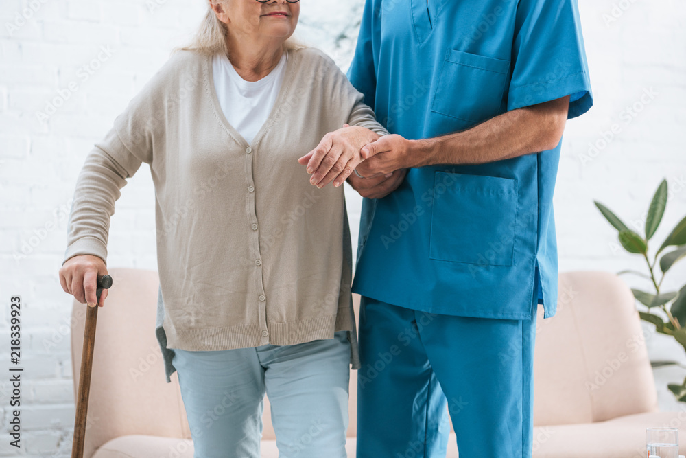 cropped shot of male nurse supporting senior woman with walking cane