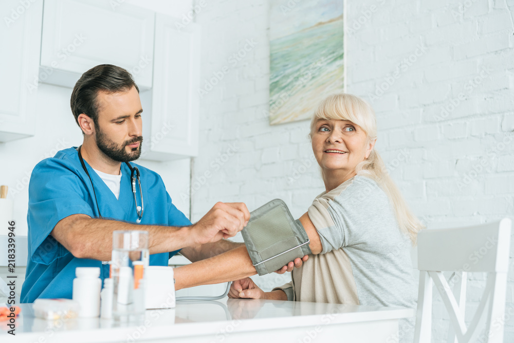 Obraz premium male nurse measuring blood pressure to smiling senior woman