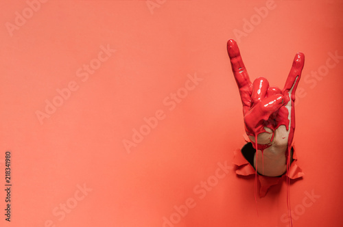Rock sign gesture painted with red paint coming out of wall
