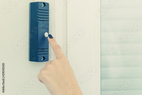 A woman's hand presses the doorphone button.