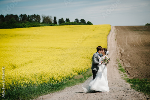 Wallpaper Mural A newlywed wedding couple embrace and kissing on a straight road, country for their honeymoon. Way on summer field of yellow rapes flowers, canola field. Torontodigital.ca