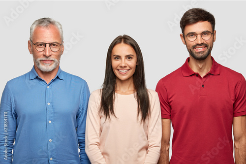 Family portrait of mature grey haired male and his attractive son, daughter, stand closely, pose for album photos, have cheerful expressions, have good relationships. People, age and family concept photo