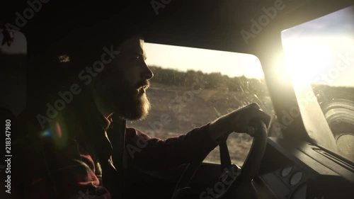 Outdoorsy man with a beard by the wheel driving a vintage 4x4, handheld, sunrise photo